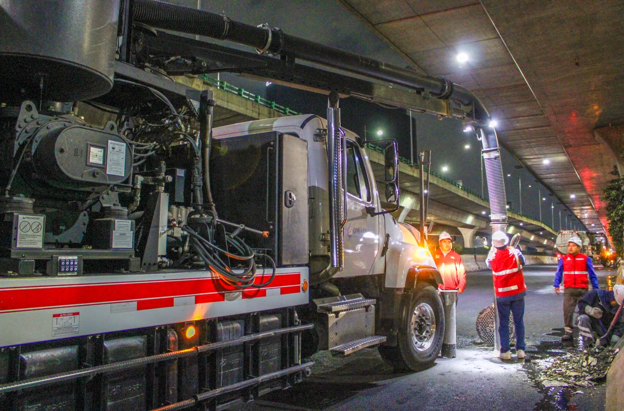 about-img-01 Des travailleurs nettoient des rues à l’aide de machines sous un passage supérieur, de nuit.